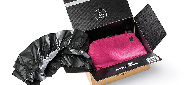 Ein Karton mit einer pinkfarbenen Tasche und schwarzen Papierpolstern