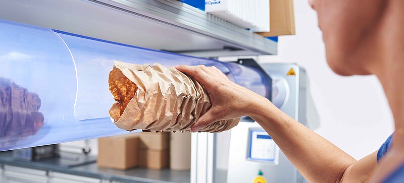 
		  A woman removing brown paper cushioning from a machine