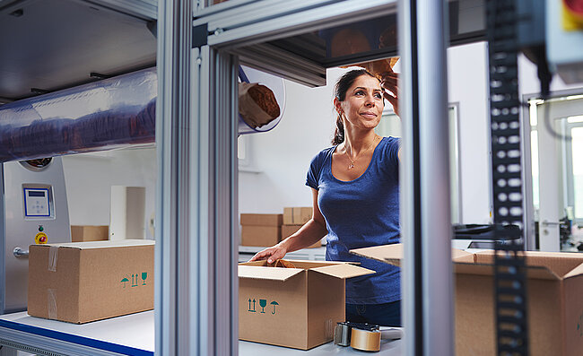 Eine Frau verpackt Produkte im Karton an einer Packstation